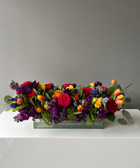 long and low floral arrangement in primary colors with see through clear vase